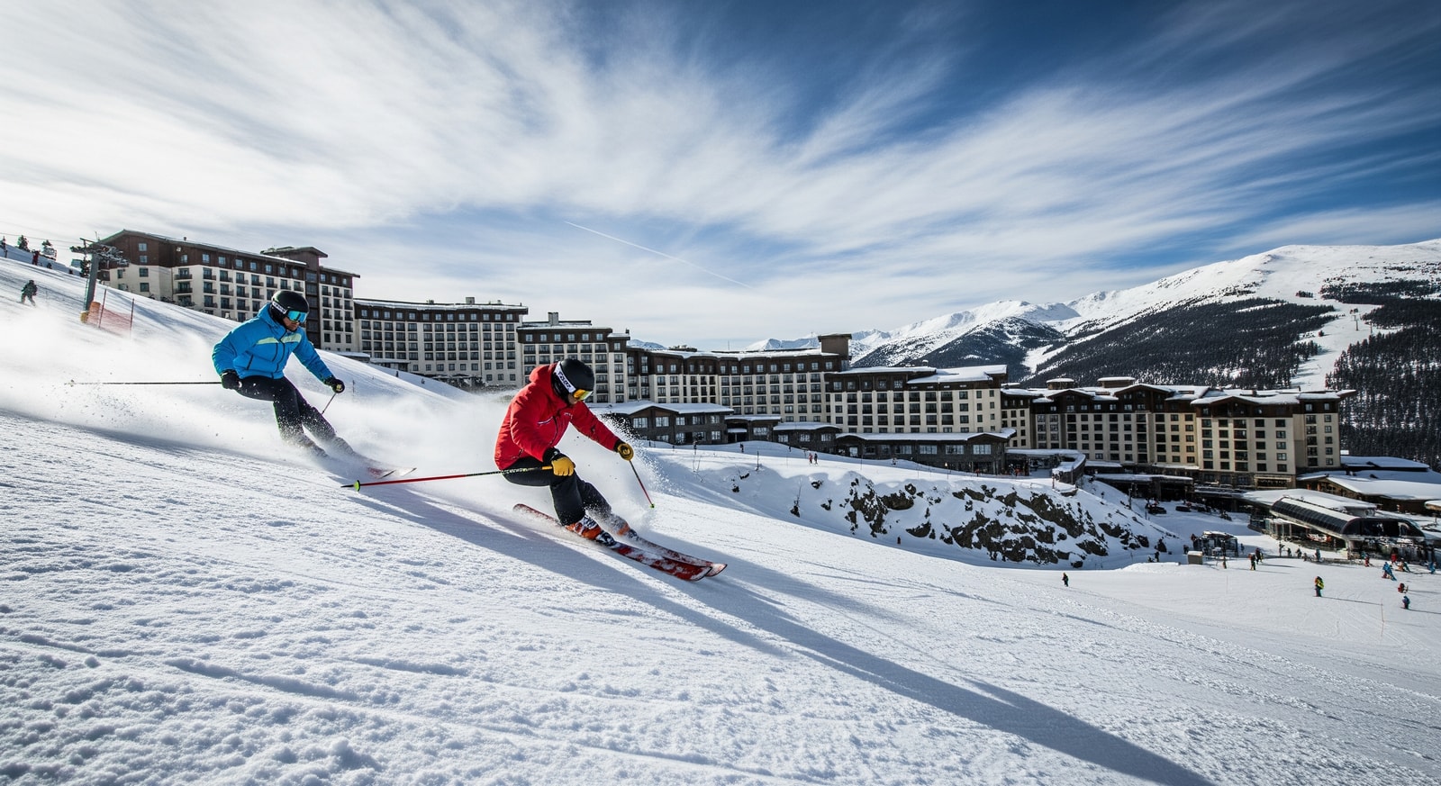 Skiers on a snowy slope with resort buildings in the background, illustrating contrasting conditions across US ski regions